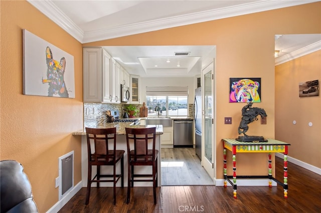 28162 Bavaria Dr, Menifee, CA 92585 - kitchen featuring stainless steel appliances, a tray ceiling, wood finished floors, ornamental molding, and a peninsula