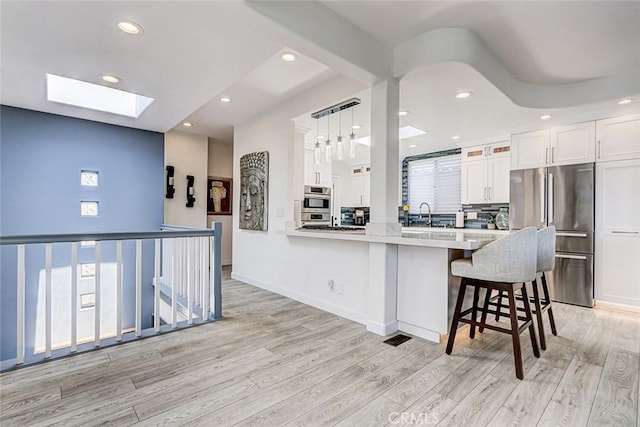 417 23rd St, Manhattan Beach, CA 90266 - kitchen with freestanding refrigerator, a breakfast bar area, a skylight, white cabinetry, and light wood finished floors