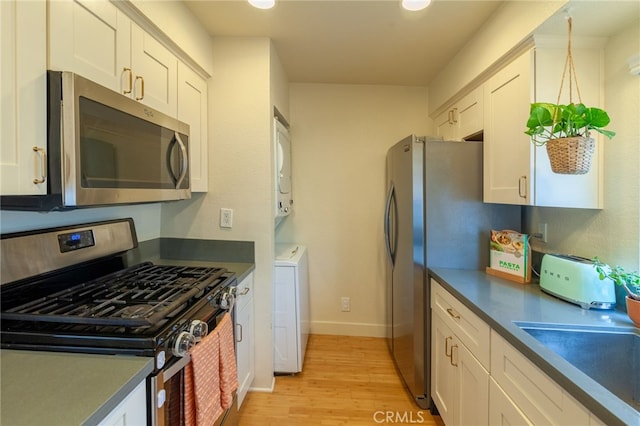 5706 Fair Ave Unit 100, North Hollywood, CA 91601 - kitchen with stainless steel appliances, dark countertops, light wood finished floors, white cabinetry, and stacked washer and clothes dryer