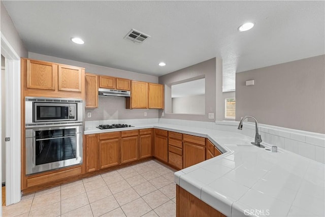 3057 Kilt Ct, Lancaster, CA 93535 - kitchen with stainless steel appliances, a sink, under cabinet range hood, tile counters, and light tile patterned floors
