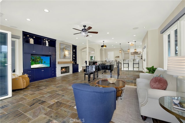 30927 Steeplechase Dr, San Juan Capistrano, CA 92675 - living area with a ceiling fan, a fireplace, stone tile floors, recessed lighting, and arched walkways