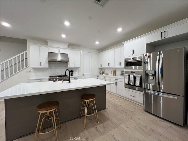 27636 Symphony Pl, Valencia, CA 91381 - kitchen featuring stainless steel appliances, under cabinet range hood, backsplash, light wood finished floors, and a kitchen breakfast bar