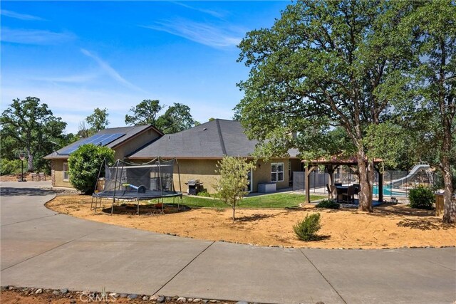 14690 Paynes Creek Rd, Red Bluff, CA 96080 - view of front of home with a trampoline, stucco siding, roof mounted solar panels, and a patio area