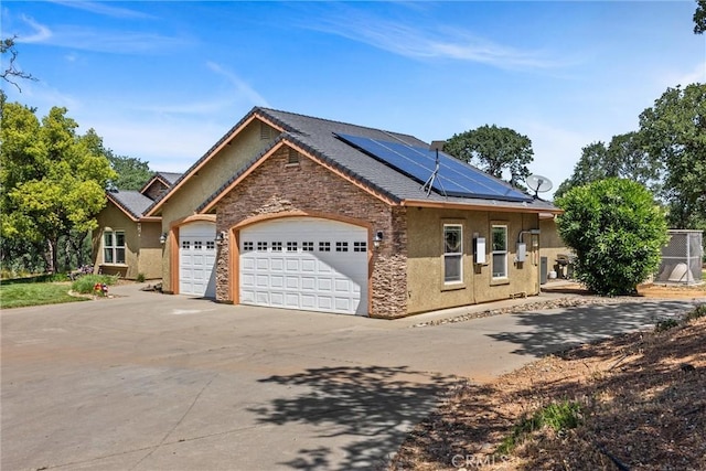 14690 Paynes Creek Rd, Red Bluff, CA 96080 - view of front facade featuring stone siding, concrete driveway, a garage, stucco siding, and roof mounted solar panels