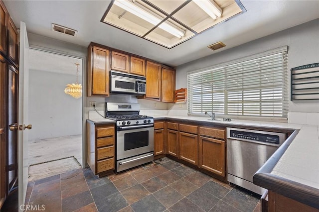1945 Cumberland Dr, West Covina, CA 91792 - kitchen featuring stainless steel appliances, brown cabinets, light countertops, dark stone finish flooring, and a sink