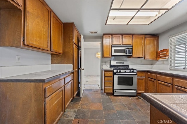 1945 Cumberland Dr, West Covina, CA 91792 - kitchen featuring stainless steel appliances, brown cabinetry, and dark stone finish flooring