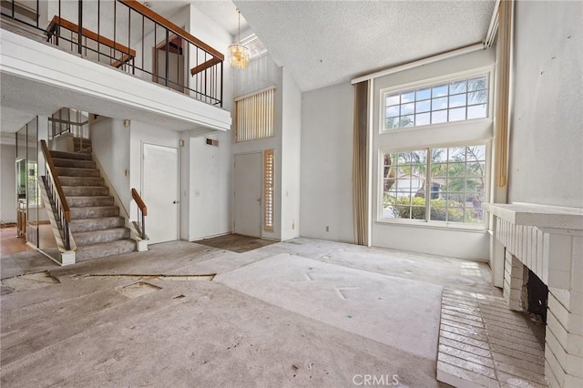 1945 Cumberland Dr, West Covina, CA 91792 - unfurnished living room with stairs, a towering ceiling, a brick fireplace, and a textured ceiling
