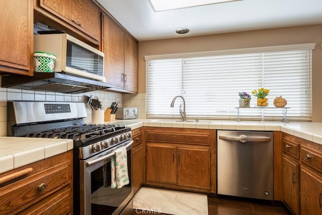 4734 E Tanglewood Ave, Anaheim, CA 92807 - kitchen featuring appliances with stainless steel finishes, a sink, backsplash, tile counters, and brown cabinets