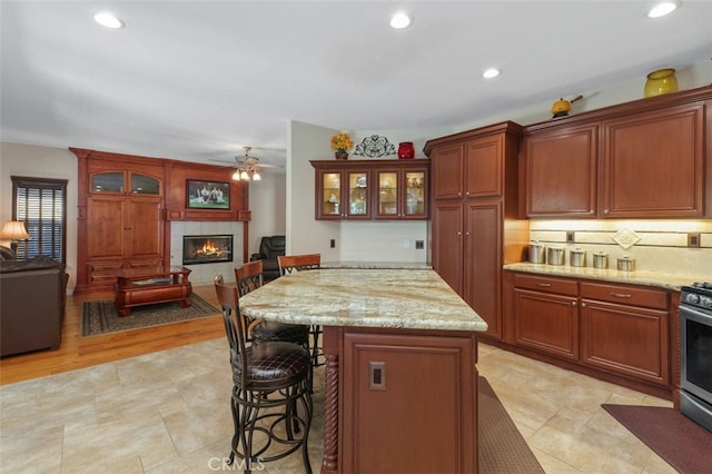 29944 Peach Tree Ct, Murrieta, CA 92563 - kitchen with a tile fireplace, a kitchen bar, open floor plan, glass insert cabinets, and ceiling fan
