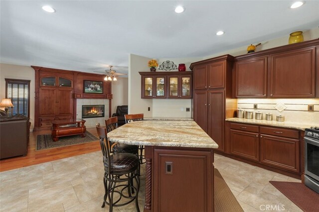 29944 Peach Tree Ct, Murrieta, CA 92563 - kitchen featuring a kitchen bar, a fireplace, open floor plan, ceiling fan, and glass insert cabinets