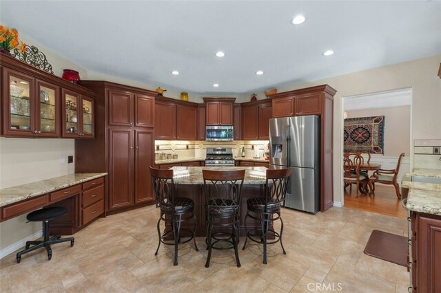 29944 Peach Tree Ct, Murrieta, CA 92563 - kitchen featuring stainless steel appliances, a kitchen breakfast bar, a kitchen island, light stone counters, and decorative backsplash