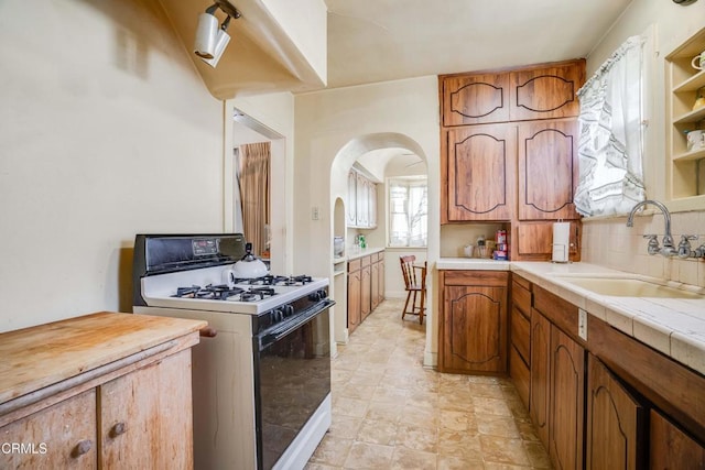 1120 S Burnside Ave, Los Angeles, CA 90019 - kitchen with range with gas stovetop, a sink, arched walkways, brown cabinets, and decorative backsplash