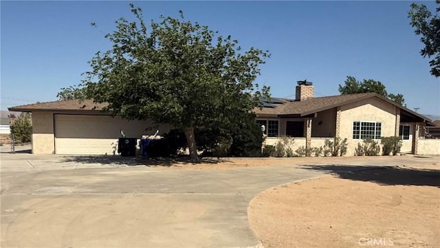 15615 Apache Rd, Apple Valley, CA 92307 - view of front facade with a chimney, stucco siding, solar panels, driveway, and a garage