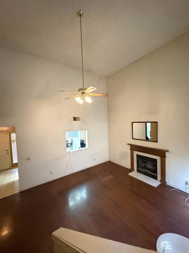 6049 N Constance Ave, Fresno, CA 93722 - unfurnished living room featuring wood finished floors, ceiling fan, a fireplace with flush hearth, and a high ceiling