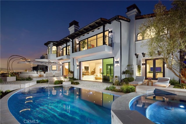17 Muir Beach Cir, Corona Del Mar, CA 92625 - back of house at night with a balcony, a chimney, a patio area, an outdoor pool, and stucco siding