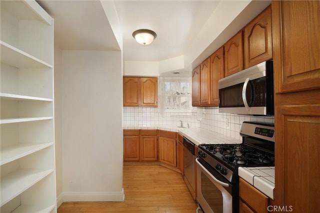 7228 Bairnsdale St, Downey, CA 90240 - kitchen featuring stainless steel appliances, tile counters, light wood-style flooring, brown cabinets, and tasteful backsplash
