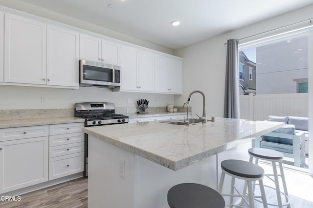 1607 Dundas Pl, Upland, CA 91784 - kitchen with stainless steel appliances, a sink, white cabinets, a breakfast bar area, and light wood-style floors