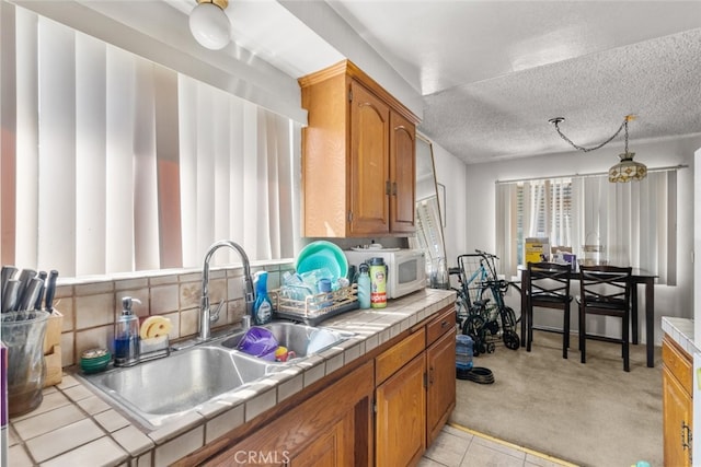 7614 Mason Ave, Winnetka, CA 91306 - kitchen featuring tile counters, a sink, light colored carpet, brown cabinetry, and a textured ceiling