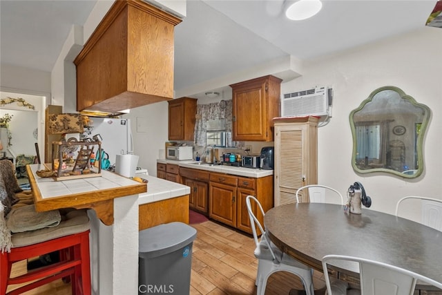 7614 Mason Ave, Winnetka, CA 91306 - kitchen with white appliances, tile countertops, light wood finished floors, brown cabinets, and a wall mounted air conditioner
