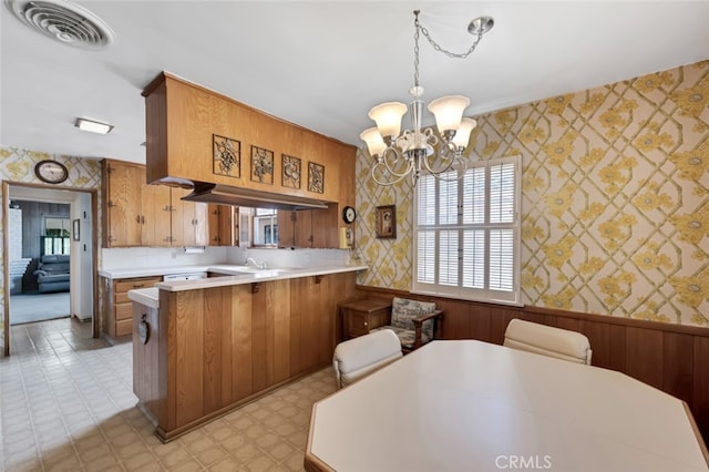 6130 Longridge Ave, Valley Glen, CA 91401 - kitchen with wallpapered walls, a chandelier, brown cabinetry, a peninsula, and light countertops