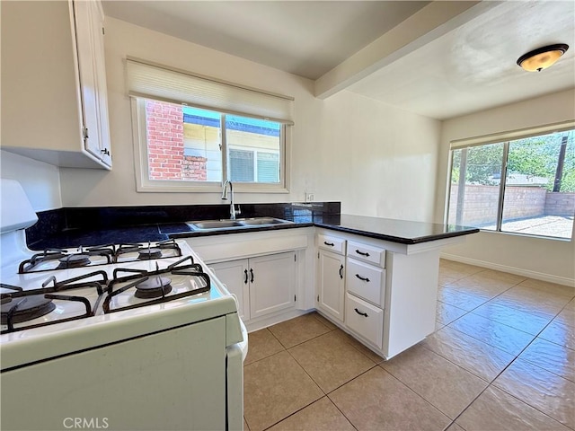 44037 Fern Ave, Lancaster, CA 93534 - kitchen with white gas stove, a sink, white cabinets, dark countertops, and a peninsula