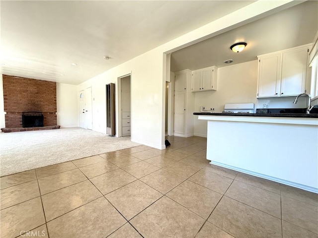 44037 Fern Ave, Lancaster, CA 93534 - kitchen with light tile patterned floors, white cabinetry, dark countertops, open floor plan, and a brick fireplace