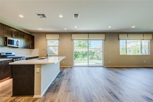 13139 Upland Ct, Hesperia, CA 92344 - kitchen featuring appliances with stainless steel finishes, a sink, light countertops, an island with sink, and dark brown cabinetry