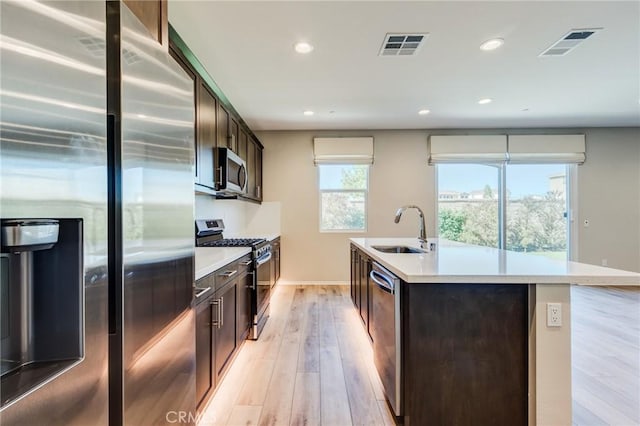 13139 Upland Ct, Hesperia, CA 92344 - kitchen featuring stainless steel appliances, a sink, dark brown cabinets, a center island with sink, and light wood finished floors