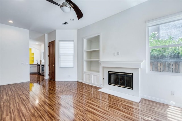 11259 Corsica Ct, Rancho Cucamonga, CA 91730 - unfurnished living room featuring a ceiling fan, built in shelves, wood finished floors, a glass covered fireplace, and recessed lighting