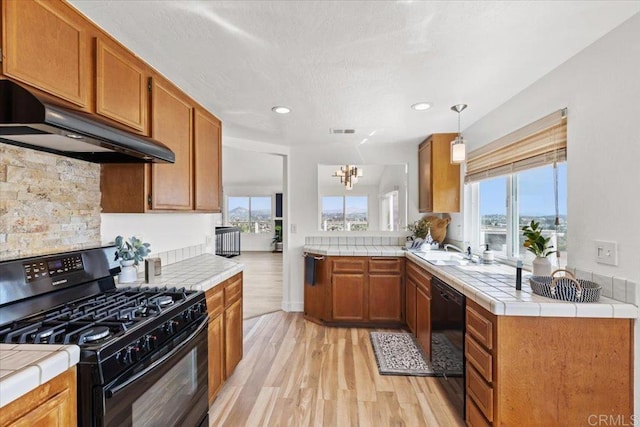 1435 Archwood Pl, Escondido, CA 92026 - kitchen with black appliances, range hood, tile counters, light wood-type flooring, and brown cabinetry