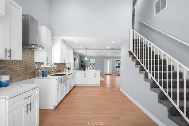 1223 W 90th St, Los Angeles, CA 90044 - kitchen featuring wall chimney exhaust hood, a peninsula, light wood-type flooring, decorative backsplash, and white cabinetry