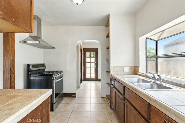 541 Randolph St, Pomona, CA 91768 - kitchen featuring stainless steel gas range oven, wall chimney range hood, tile countertops, arched walkways, and light tile patterned floors