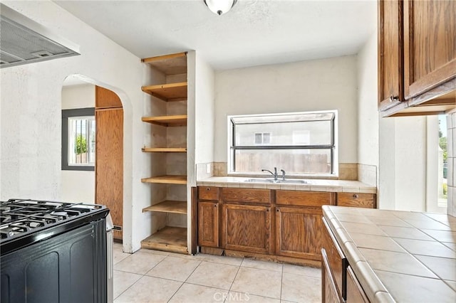 541 Randolph St, Pomona, CA 91768 - kitchen with tile counters, range hood, open shelves, arched walkways, and brown cabinets