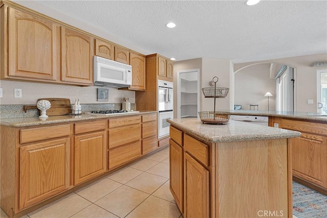 19410 Allegheny Ct, Apple Valley, CA 92307 - kitchen featuring white appliances, a textured ceiling, a kitchen island, light stone counters, and arched walkways