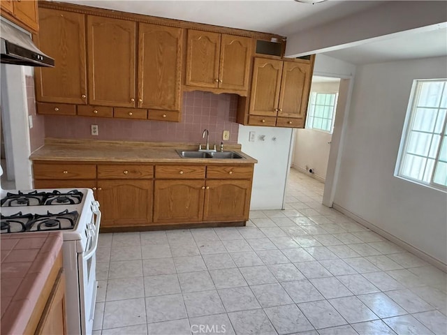 4639 Flora St, Montclair, CA 91763 - kitchen with a sink, under cabinet range hood, white gas stove, brown cabinets, and tile counters