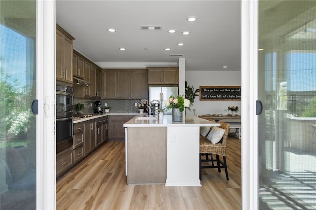 32325 Hillstone St, Temecula, CA 92591 - kitchen with light wood-type flooring, appliances with stainless steel finishes, backsplash, a kitchen island with sink, and light countertops