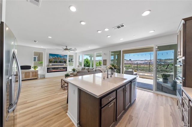 32325 Hillstone St, Temecula, CA 92591 - kitchen with appliances with stainless steel finishes, dark brown cabinetry, light wood-style flooring, light countertops, and a kitchen island with sink