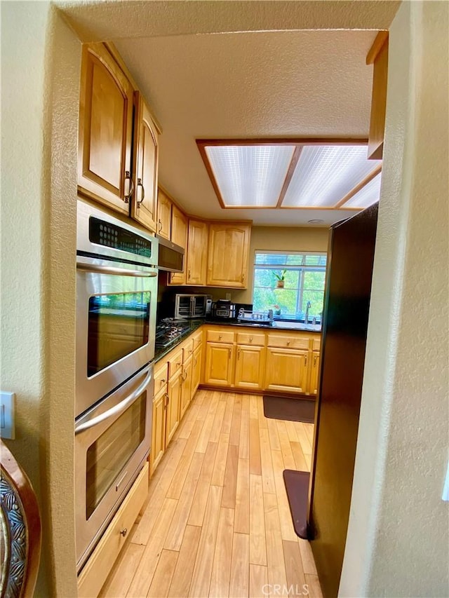 5218 Rocky Mountain Pl, Rancho Cucamonga, CA 91737 - kitchen featuring appliances with stainless steel finishes, light wood finished floors, dark countertops, light brown cabinetry, and a textured wall