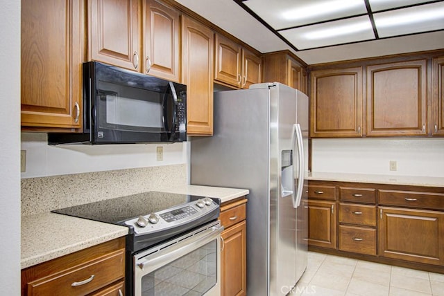 3375 Punta Alta Unit A, Laguna Woods, CA 92637 - kitchen with black microwave, stainless steel electric stove, brown cabinetry, and light tile patterned flooring