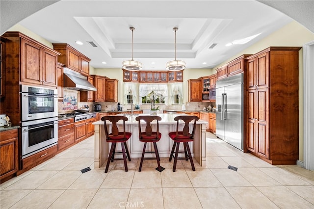 37626 Via Majorca, Murrieta, CA 92562 - kitchen featuring appliances with stainless steel finishes, under cabinet range hood, backsplash, a tray ceiling, and a kitchen island