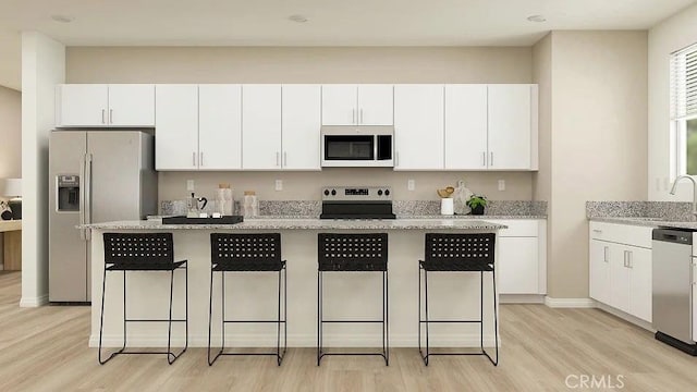 24943 Sirius St, Moreno Valley, CA 92551 - kitchen with appliances with stainless steel finishes, light wood-style floors, white cabinets, a kitchen breakfast bar, and a sink