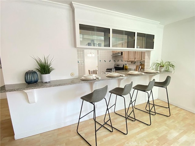 619 Center St, El Segundo, CA 90245 - kitchen featuring stainless steel range, a kitchen bar, tasteful backsplash, glass insert cabinets, and under cabinet range hood