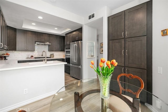 3510 Lilac Ave Unit 13, Corona Del Mar, CA 92625 - kitchen with stainless steel appliances, under cabinet range hood, dark brown cabinetry, light wood-style flooring, and decorative backsplash