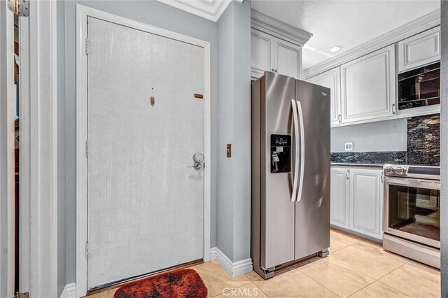 5927 E Creekside Ave Unit 18, Orange, CA 92869 - kitchen featuring appliances with stainless steel finishes, light tile patterned floors, dark stone counters, ornamental molding, and white cabinetry