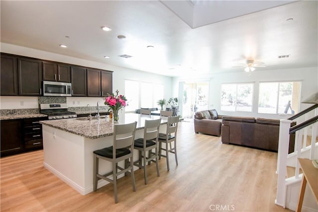 24649 Round Meadow Dr, Menifee, CA 92584 - kitchen featuring appliances with stainless steel finishes, a kitchen bar, light wood-type flooring, a kitchen island with sink, and a sink