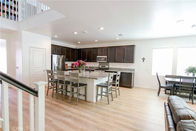 24649 Round Meadow Dr, Menifee, CA 92584 - kitchen with stainless steel appliances, a kitchen bar, light wood-style floors, dark brown cabinets, and recessed lighting