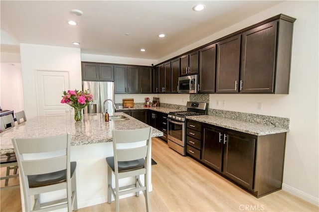 24649 Round Meadow Dr, Menifee, CA 92584 - kitchen featuring appliances with stainless steel finishes, a sink, light wood-style floors, a kitchen bar, and dark brown cabinets