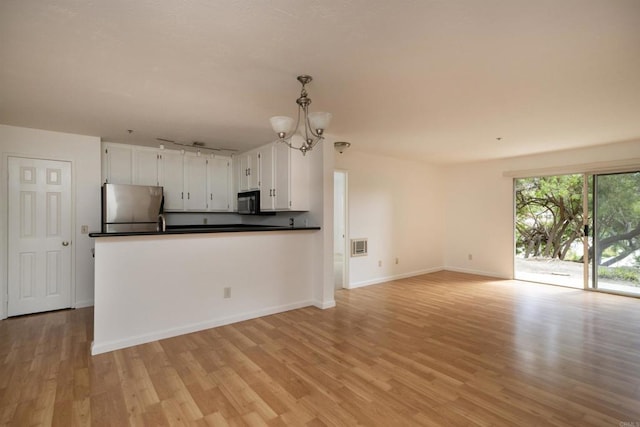 7753 Caminito Encanto Unit 102, Carlsbad, CA 92009 - kitchen with freestanding refrigerator, dark countertops, a chandelier, light wood-type flooring, and white cabinets