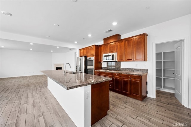 6864 Ripple Ct, Jurupa Valley, CA 91752 - kitchen featuring appliances with stainless steel finishes, a sink, light wood-style flooring, a center island with sink, and a lit fireplace