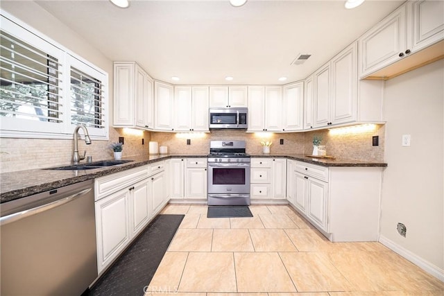 11015 Charleston St, Rancho Cucamonga, CA 91701 - kitchen featuring appliances with stainless steel finishes, a sink, decorative backsplash, dark stone countertops, and white cabinetry
